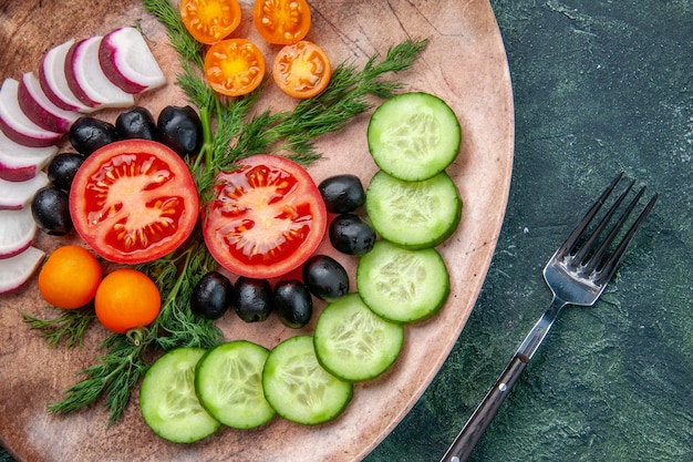 Close up view of fresh chopped vegetables olives in a brown plate and fork on green black mixed colors background