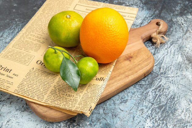 반으로 자른 나무 커팅 보드에 잎과 신문이 있는 신선한 감귤류 과일의 클로즈업 보기 회색 테이블