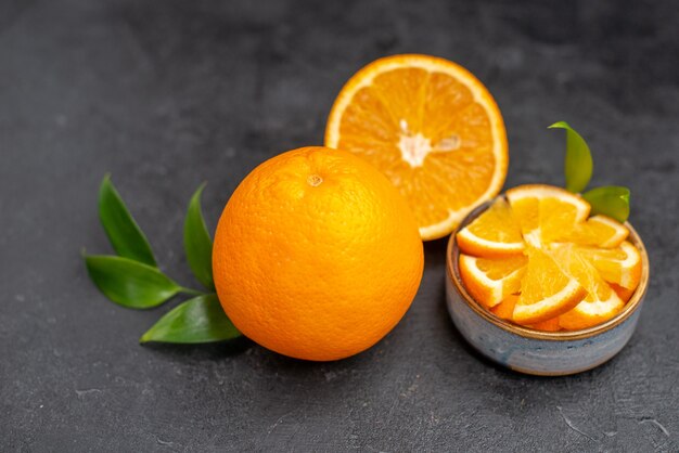 Close up view of fresh cut orange halves on whole lemons on dark table