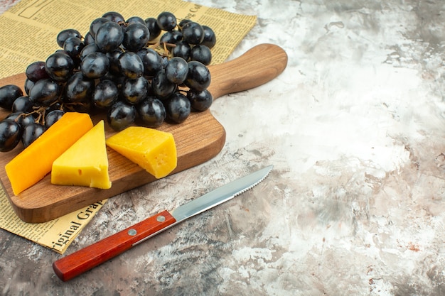 Foto gratuita vista ravvicinata del delizioso grappolo di uva nera fresca e di vari tipi di formaggio su tagliere di legno e coltello su sfondo di colore misto