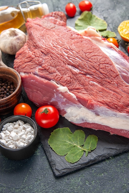 Close up view of fresh raw red meat on black tray pepper vegetables fallen oil bottle knife on dark color background