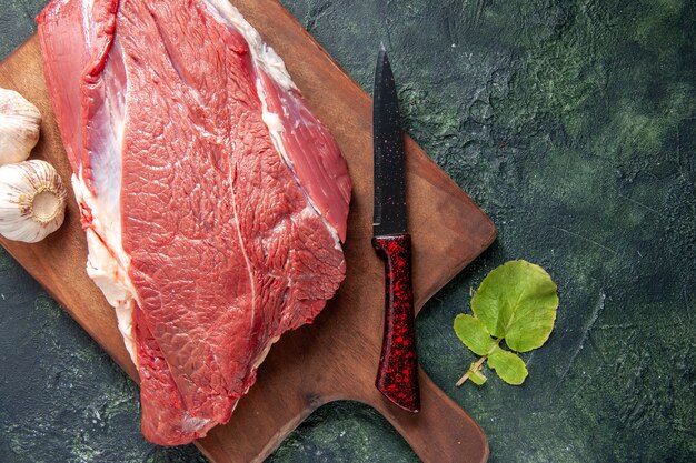 Close up view of fresh raw red meats on brown wooden cutting board and knife garlics on dark color background