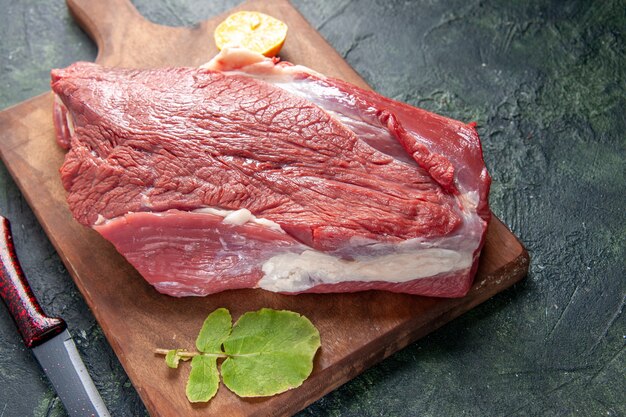 Close up view of fresh raw red meats lemon on brown wooden cutting board and knife on dark color background