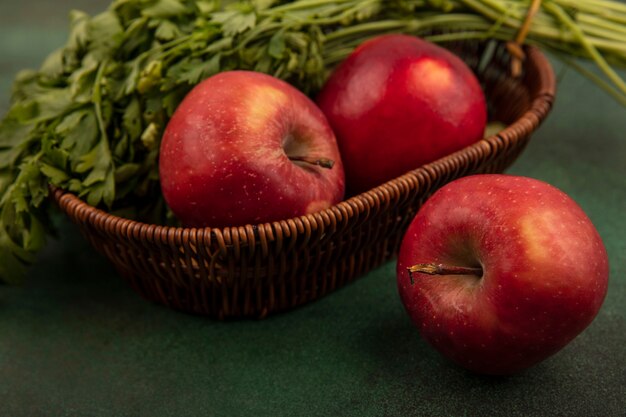 Крупным планом вид свежих красных яблок и петрушки на ведре на зеленой поверхности