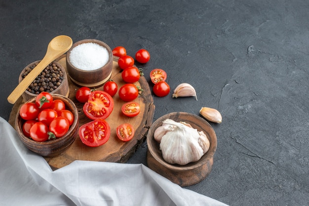 Close up view of fresh tomatoes and spices on wooden board white towel garlics on black surface