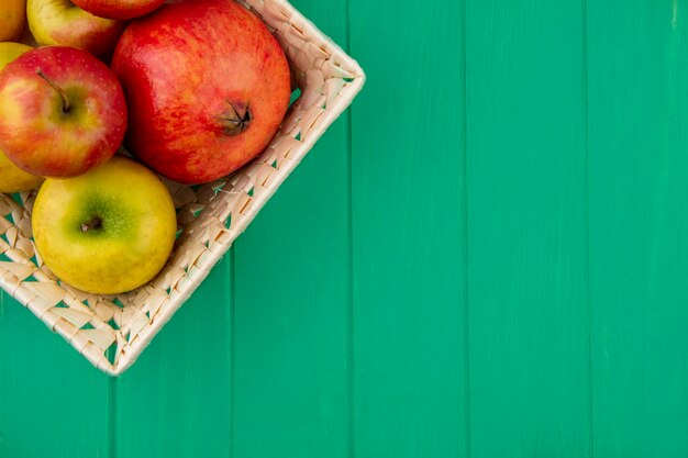 Крупным планом вид фруктов, как гранат и яблоки в корзине на зеленой поверхности
