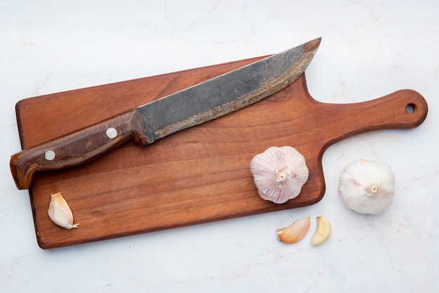 Close-up view of garlic with knife on cutting board on white background