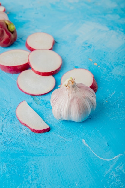Close-up view of garlic with sliced radish on blue background with copy space