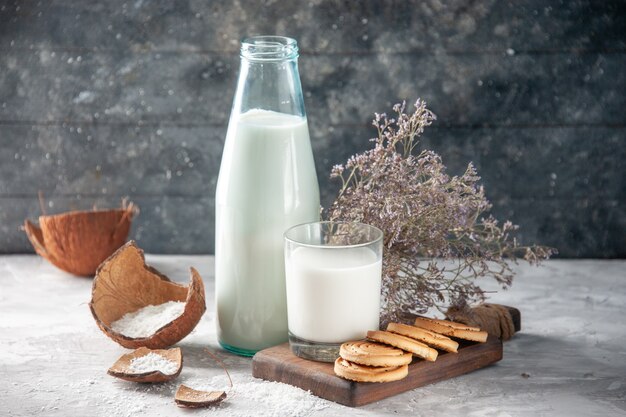 Close up view of glass bottle and cup filled with milk on wooden tray flower on dark background