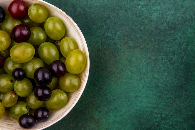 Close-up view of grape berries in bowl on green background with copy space