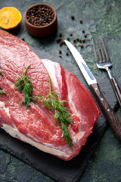 Close up view of green on fresh red raw meat cutlery set on cutting board and pepper lemon on green black mix color background