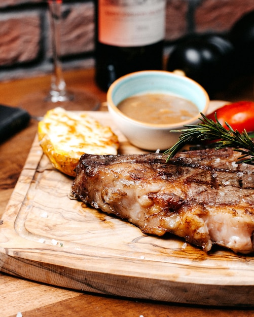 Close up view of griled beef steak served with vegetables and sauce on wooden board