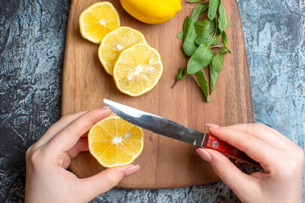 Крупным планом вид руки, рубящей свежие лимоны и мяту на деревянной разделочной доске на темном фоне