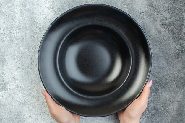 Close up view of hand holding black dinnerware set on isolated gray ice surface with free space