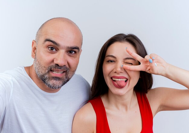 Close-up view of happy adult couple woman winking showing tongue doing peace sign both looking 