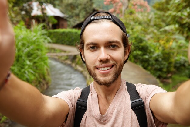 Close up view of happy face of attractive hiker with beard smiling while taking selfie