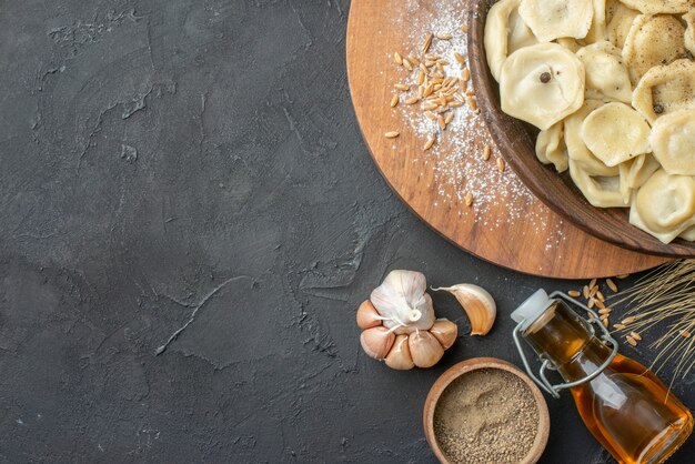 Close up view of homemade dumplings in a brown bowl on a wooden cutting board spikes garlics pepper fallen oil bottle on dark table with free space