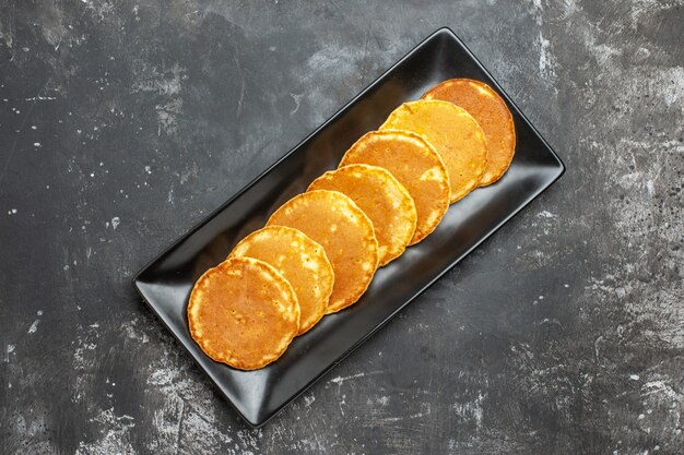 Close up view of homemade pancakes lined up on a square shaped black plate on gray