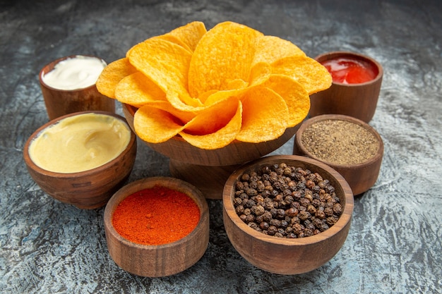 Close up view of homemade potato chips decorated like flower shaped different spices mayonnaise and ketchup on gray table