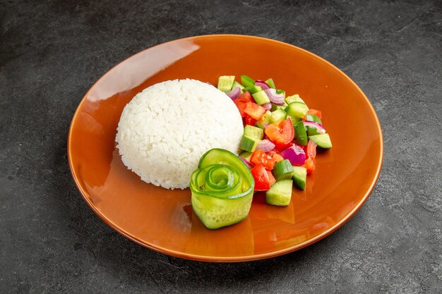 Close up view of homemade rice dish and salad with tomato and cucumber on dark