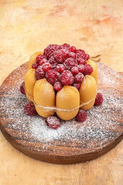 Close up view of homemade soft cake with fruits on wooden cutting board on mixed color table