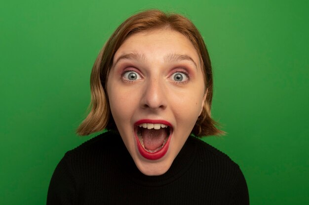 Close-up view of impressed young blonde girl  isolated on green wall