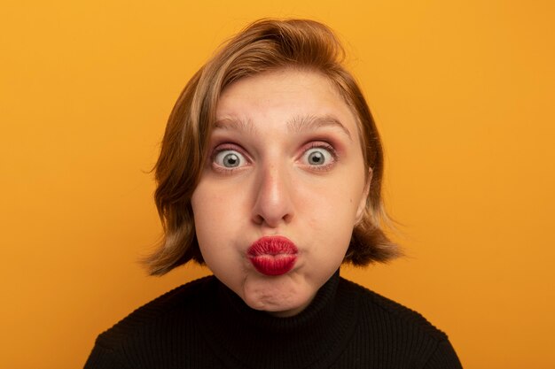 Close-up view of impressed young blonde girl puffing her cheeks 