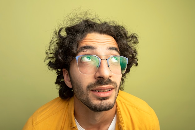 Free photo close-up view of impressed young handsome caucasian man looking up wearing glasses isolated on olive green wall