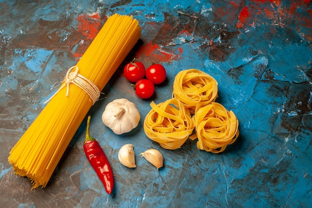 Close up view of Italian various pastas for dinner preparation garlics peppers tomatoes onions on blue background