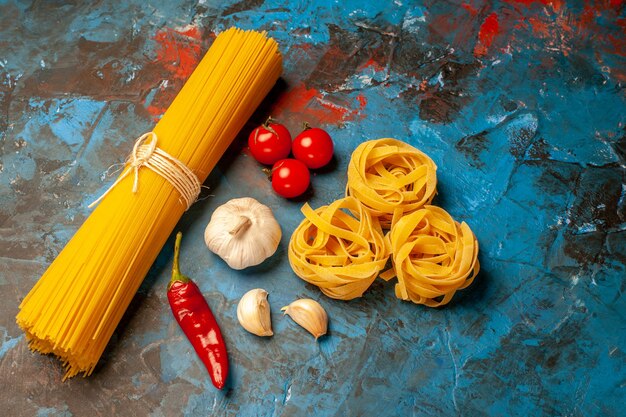 파란색 배경에 저녁 준비 마늘 고추 토마토 양파를 위한 이탈리아의 다양한 파스타를 가까이서 볼 수 있습니다.