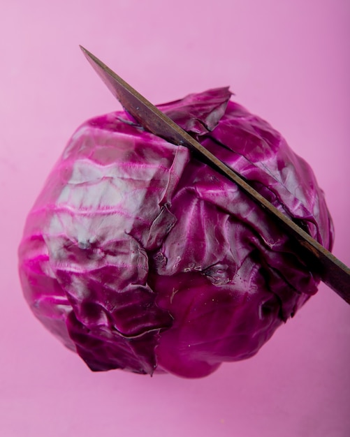 Взгляд конца-вверх ножа режа фиолетовую капусту на фиолетовой предпосылке