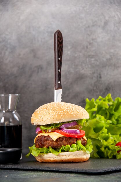 Close up view of knife in delicious meat sandwich and green pepper on black tray sauce tomatoes with stem on gray surface