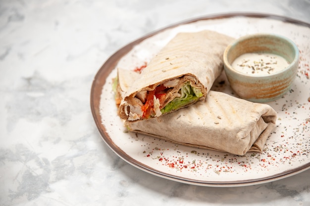 Close up view of lavash wrap and yogurt in a small bowl on a plate on stained white surface with free space