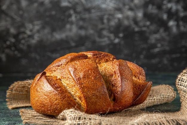 Close up view of a loaf of dietary black bread on brown towel on dark colors surface with free space