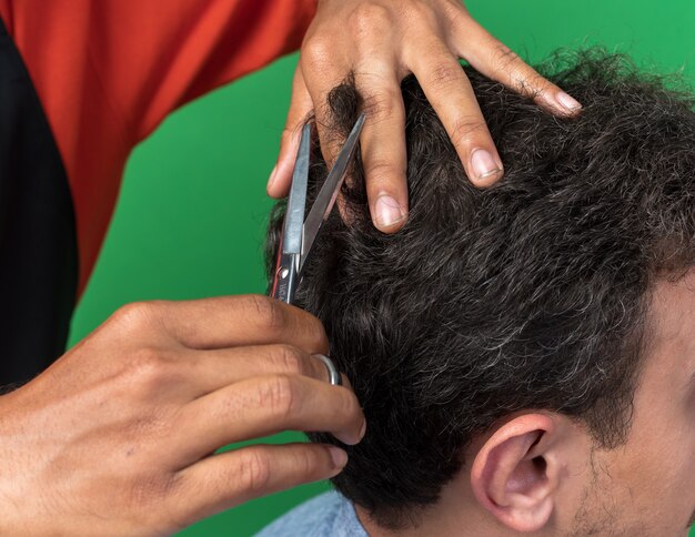 Foto gratuita vista ravvicinata delle mani del barbiere maschio che fanno taglio di capelli per il suo giovane cliente