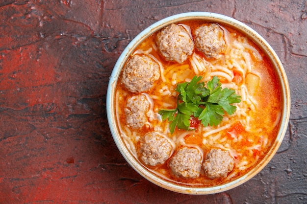 Close up view of meatballs soup with noodles in a brown bowl on the left side of dark background
