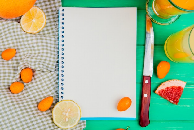 Free photo close-up view of note pad with orange lemon kumquat grapefruit knife and juices around on green background with copy space