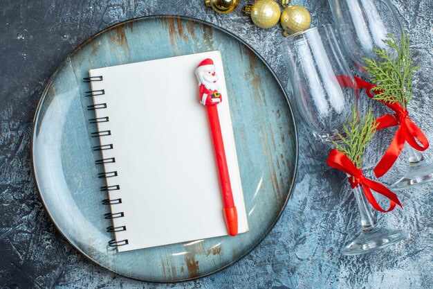 Close up view of a notebook with pen on blue plate and fallen glass goblets next to decoration accessories on dark background