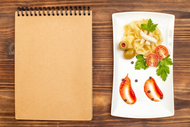 갈색 나무 표면에 있는 흰색 접시 노트북에 야채와 함께 제공되는 맛있는 파스타 식사의 클로즈업