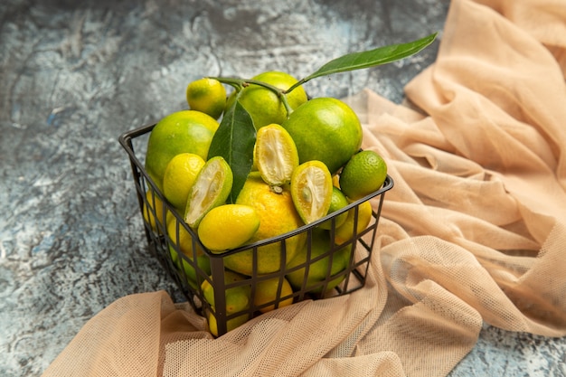 Крупным планом вид свежих кумкватов и лимонов в черной корзине на полотенце на сером фоне