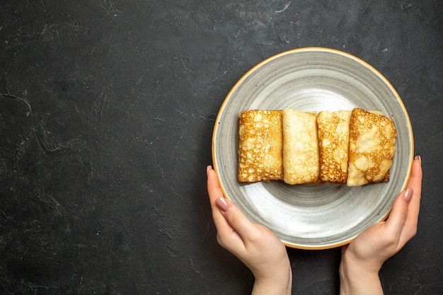 검은 배경에 흰색 접시에 맛있는 고기로 채워진 팬케이크를 들고 손의 보기를 닫습니다