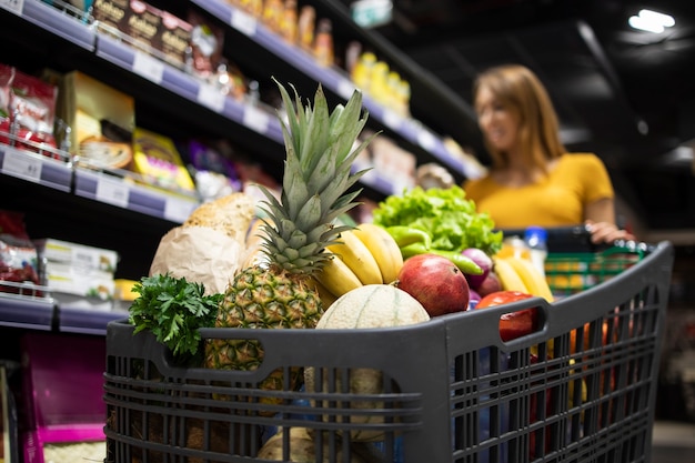 無料写真 バックグラウンドで女性が製品を選択している間、食べ物でいっぱいのショッピングカートのクローズアップビュー