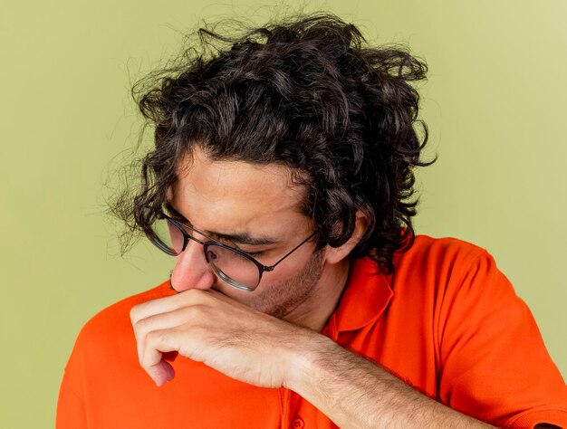 Бесплатное фото Крупным планом вид молодого больного человека в очках, вытирающего нос рукой с закрытыми глазами, изолированного на оливково-зеленой стене