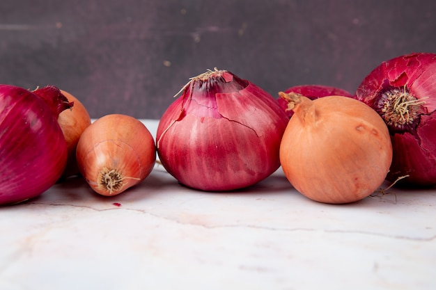Close-up view of onions on white surface and maroon background