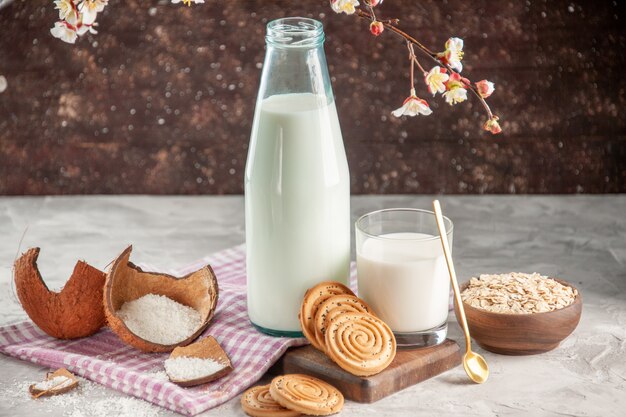 Close up view of open glass bottle and cup filled with milk spoon cookies oats in brown pot on purple stripped towel on wooden cutting board