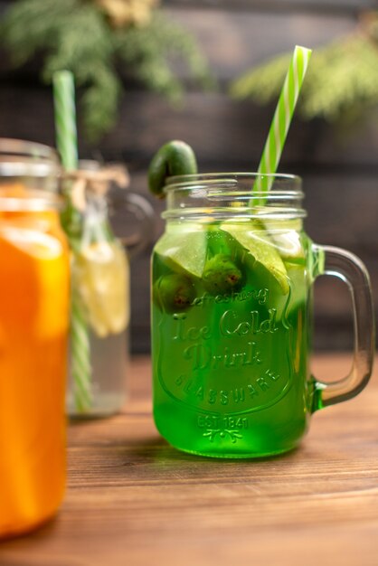 Close up view of organic fresh juices in bottles served with tubes and fruits on a brown wooden table