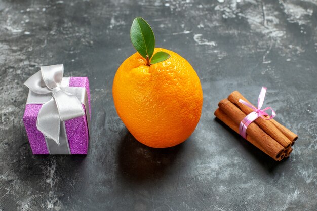 Close up view of organic fresh orange with stem and leaf near a gift and cinnamon limes on dark background