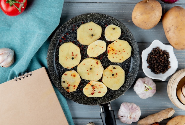 Close up view of pan full of potato slices with black pepper garlic ginger on wooden background