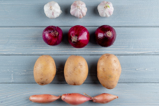 Free photo close up view of pattern of vegetables as garlic onion potato shallot on wooden background with copy space