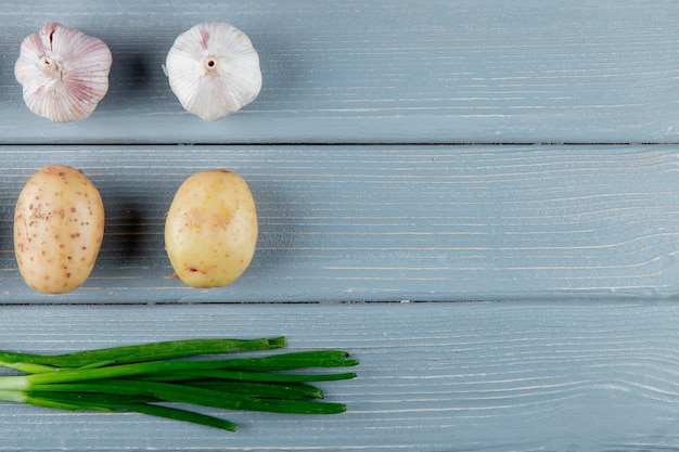 Free photo close up view of pattern of vegetables as garlic potato and green onion on wooden background with copy space